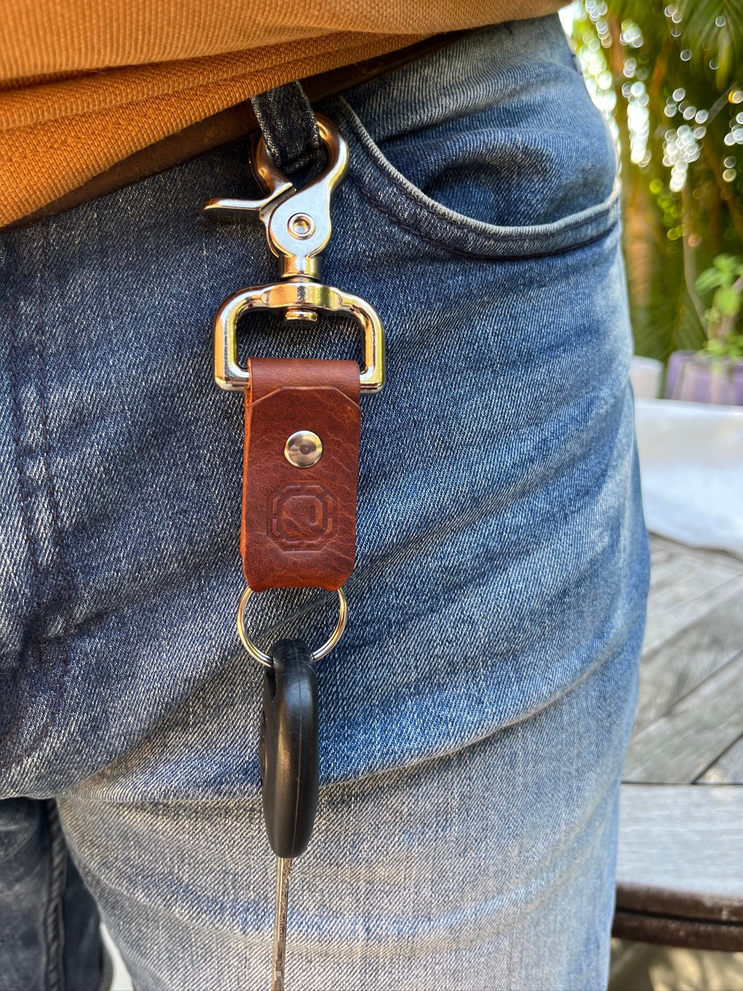 Close-up of a leather strap with silver hardware on a person's leg, with a blurred outdoor background.