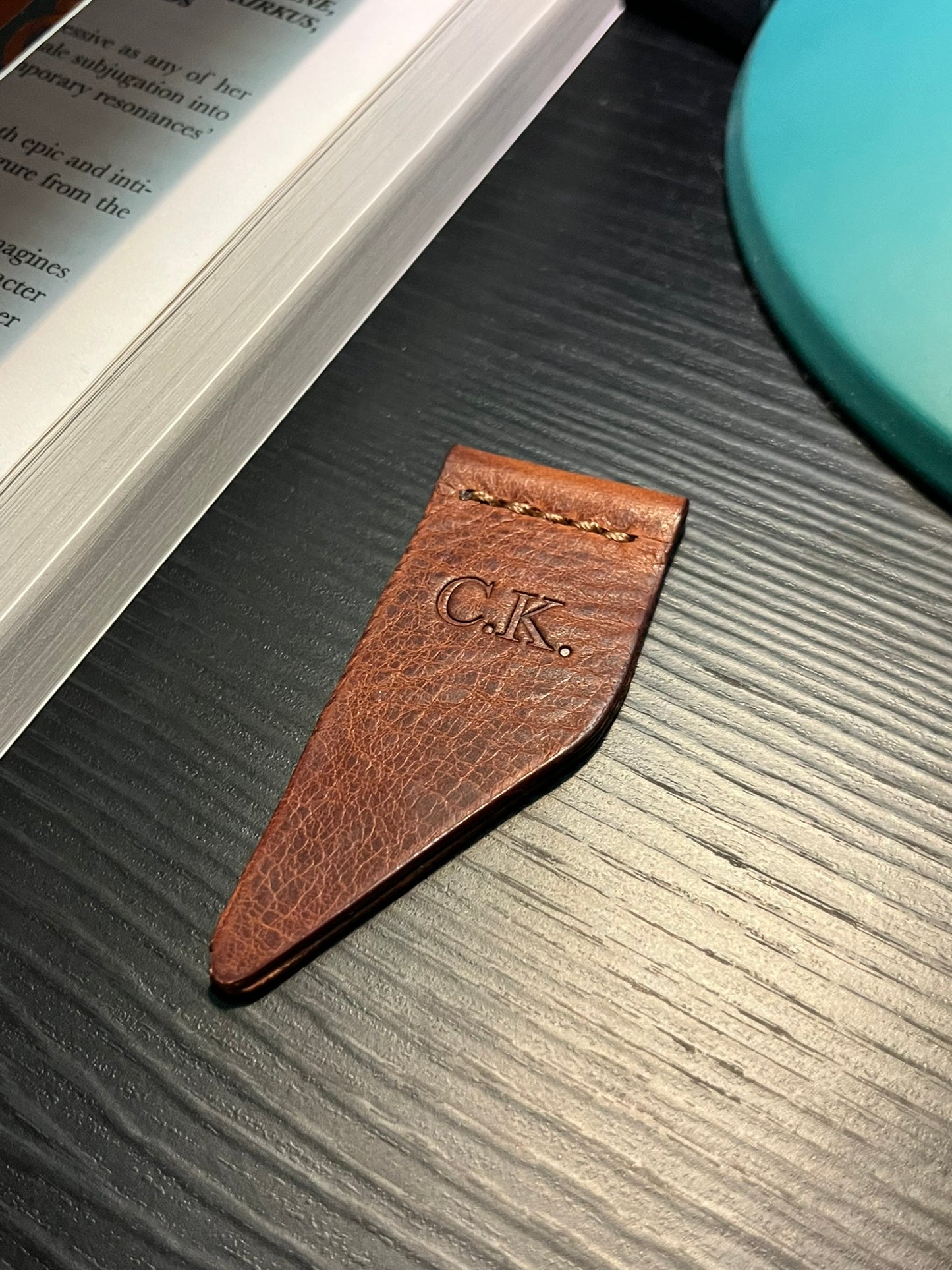 Cognac brown leather bookmark with debossed initials 'C.K.' on a textured surface