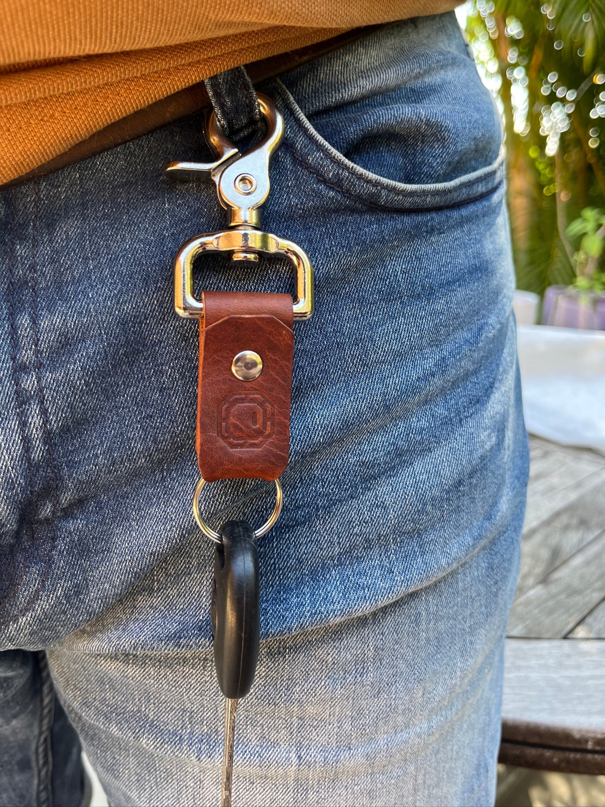 Close-up of a leather strap with silver hardware on a person's leg, with a blurred outdoor background.