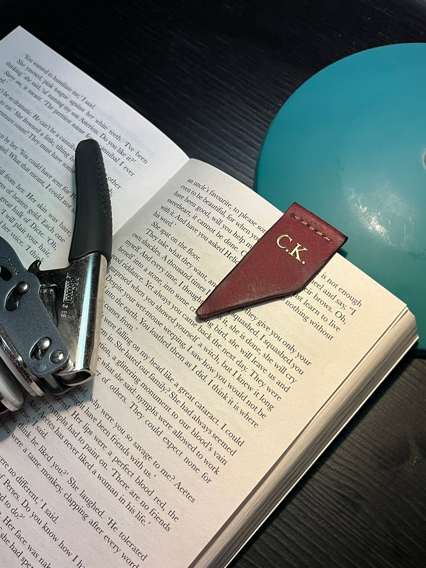 Leather bookmark with initials 'C.K.' on an open book with a book embosser.
