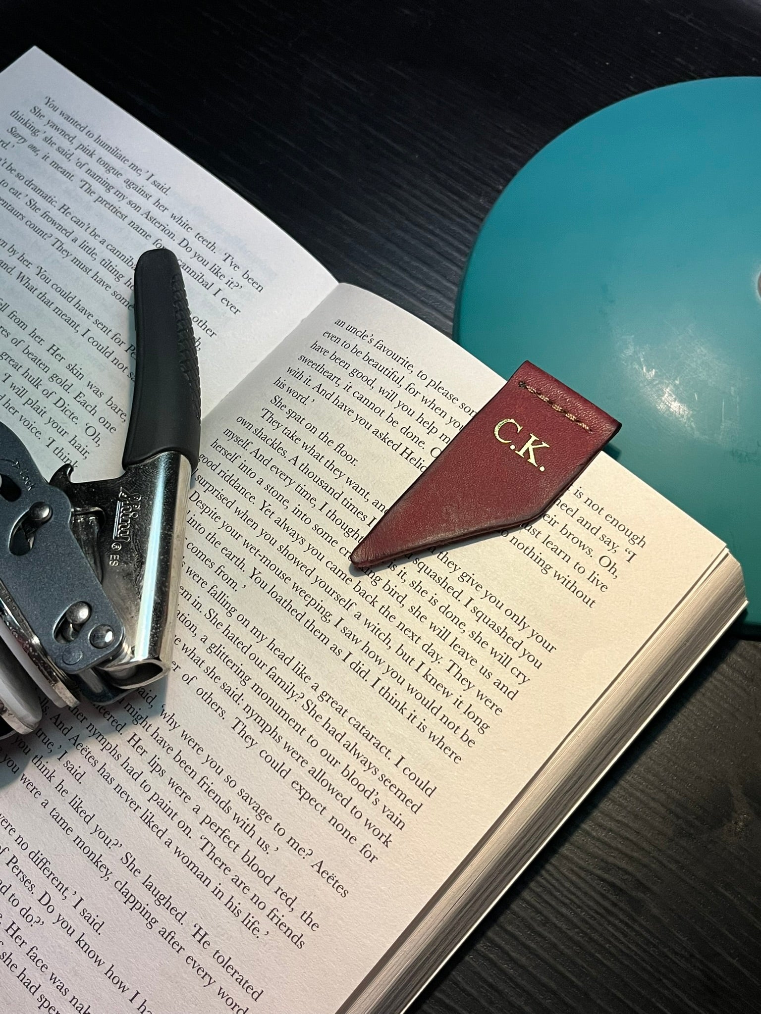 Leather bookmark with initials 'C.K.' on an open book with a book embosser.