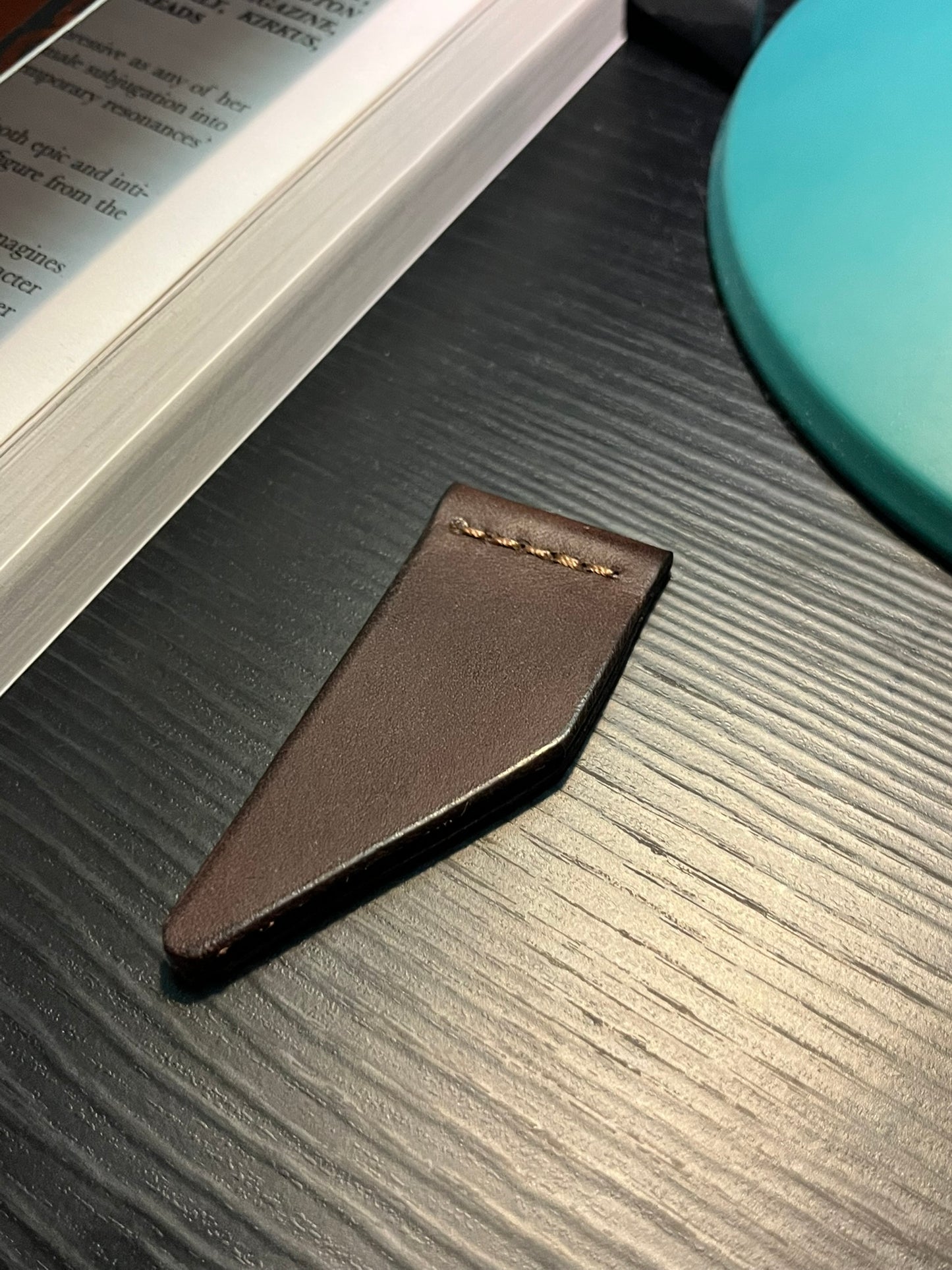 Dark brown Minerva leather ribbon-style bookmark on a textured surface with a book in the background