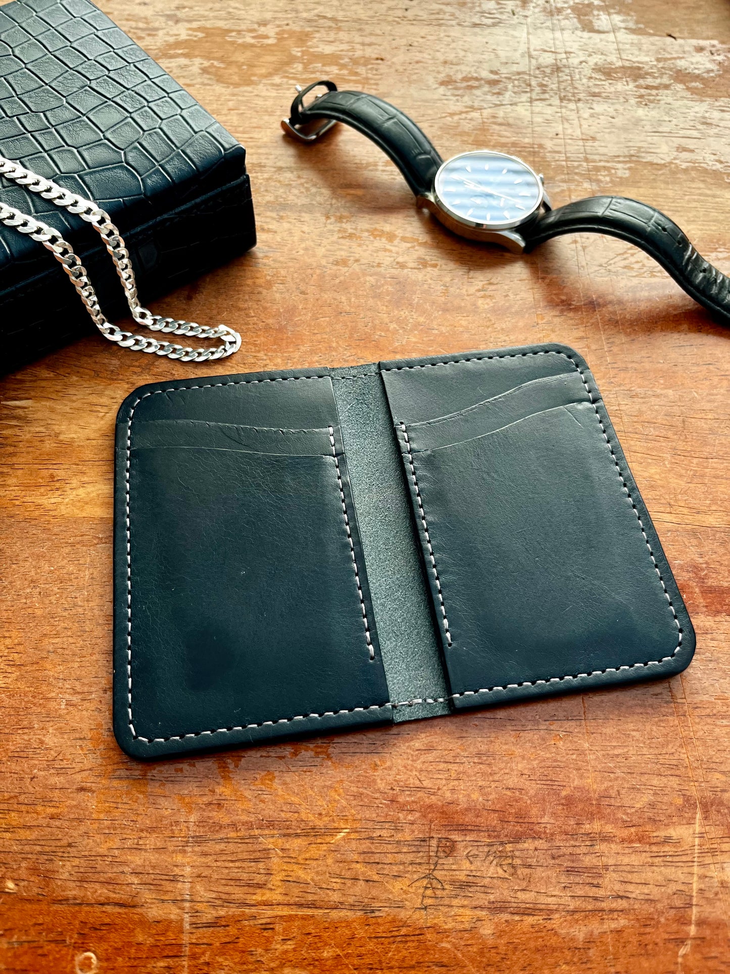 Navy leather wallet on a wooden surface with a watch and chain in the background